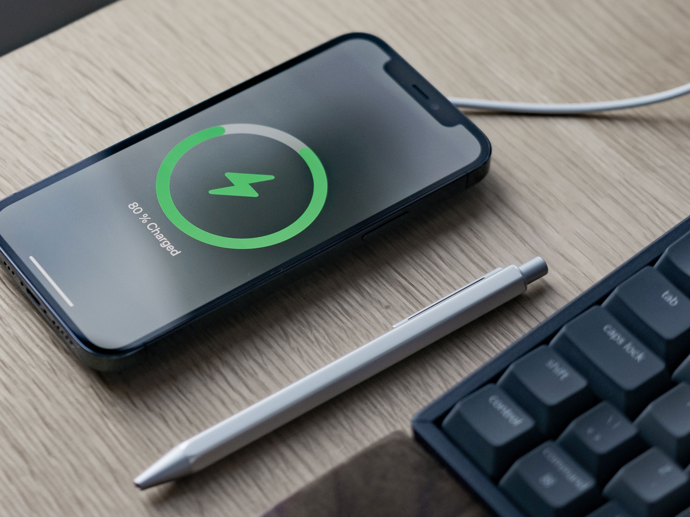 Mobile phone charging on desk next to computer keyboard