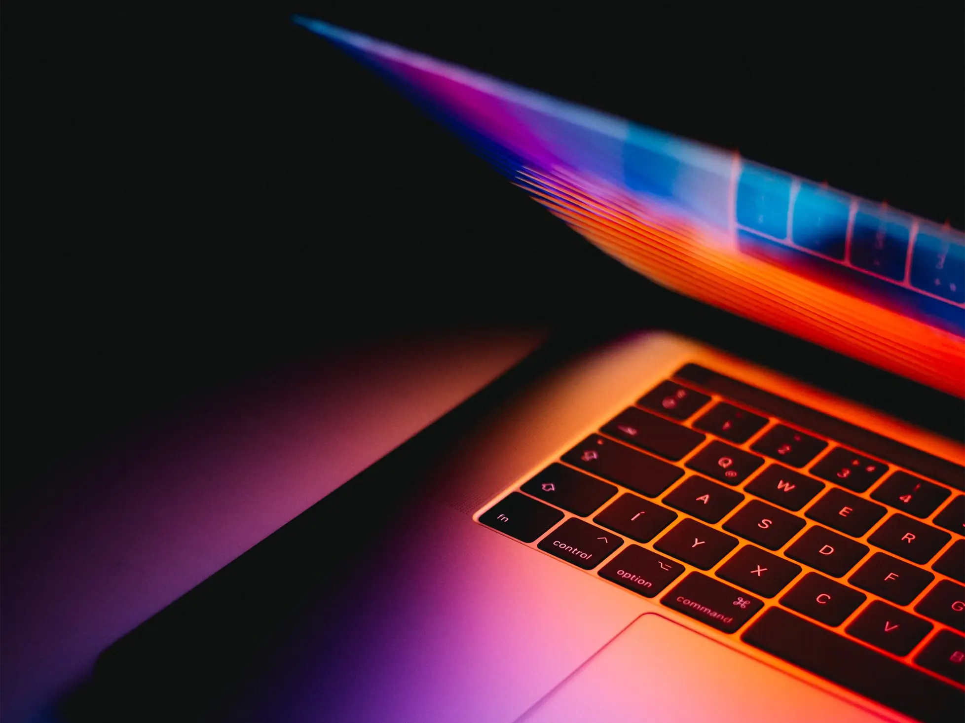 Half-closed laptop in the dark with a colourful screen glow